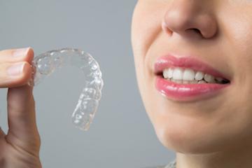 Woman holding clear plastic aligner l Invisalign Moline IL